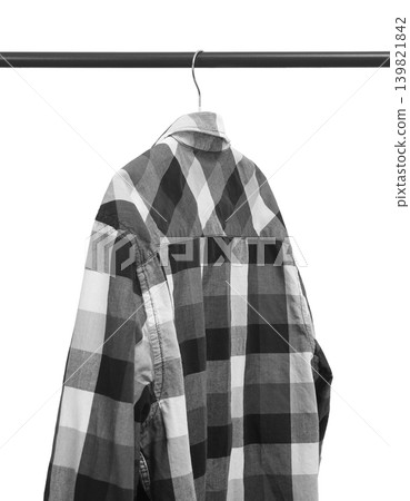Black and white plaid shirt hangs on metal rail against white background. Checkered garment rests on hanger forming clean wardrobe display. Minimalist retail fashion concept for boutique Black and white plaid shirt hangs on metal rail against white background. Checkered garment rests on hanger forming clean wardrobe display. Minimalist retail fashion concept for boutique 139821842