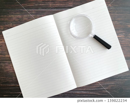 A notebook and a magnifying glass placed on a wooden table A notebook and a magnifying glass placed on a wooden table 139822234