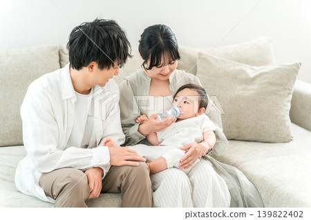 一個嬰兒坐在家裡的沙發上用奶瓶喝牛奶。 一個嬰兒坐在家裡的沙發上用奶瓶喝牛奶。 139822402