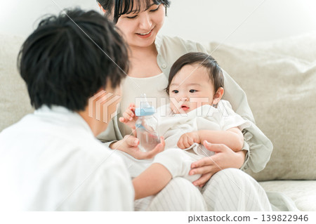 一位母親、一位媽媽和一家人坐在家裡的沙發上,用奶瓶餵寶寶。 一位母親、一位媽媽和一家人坐在家裡的沙發上,用奶瓶餵寶寶。 139822946