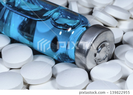 Medical bottle with blue vaccine surrounded by white pills Medical bottle with blue vaccine surrounded by white pills 139822955