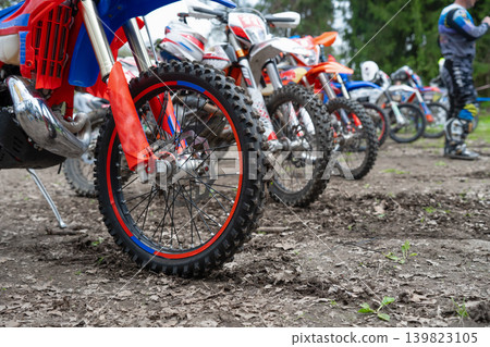 A row of modern enduro motorcycles with knobby tires parked on a dirt trail in the forest before an off-road race. 139823105