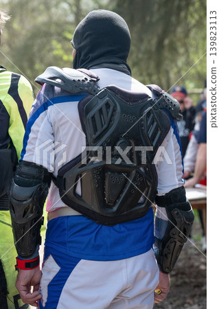 Close-up of a motocross rider from behind wearing professional body armor, chest protector and elbow pads during enduro competition. Close-up of a motocross rider from behind wearing professional body armor, chest protector and elbow pads during enduro competition. 139823113