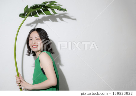 一位笑容甜美的日本女子用龜背竹葉子當傘；在傘和夏日自然風光的映襯下，她的上半身直視著鏡頭。 139823922