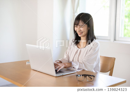 A young Japanese woman working on a computer at her desk. A young Japanese woman working on a computer at her desk. 139824323