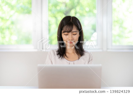A young Japanese woman working on a computer at her desk. A young Japanese woman working on a computer at her desk. 139824329