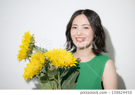 一位日本女性面帶微笑，手持向日葵，展現出夏日的美麗和明媚的生活方式，直視鏡頭。 139824458