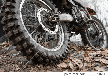 Muddy motorcycle wheel with brake disc and chain in the woods. Gritty details of an enduro bike after a ride through mud and autumn leaves. Muddy motorcycle wheel with brake disc and chain in the woods. Gritty details of an enduro bike after a ride through mud and autumn leaves. 139824611