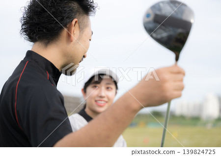 A smiling woman learning golf; a communication image of her receiving swing lessons from a golf instructor. 139824725
