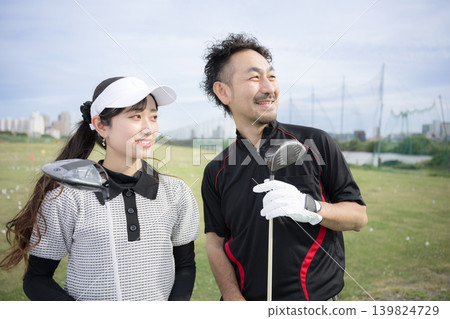 一位微笑的女士正在上高爾夫球課;她和她的高爾夫教練一起抬頭看著球門。 一位微笑的女士正在上高爾夫球課;她和她的高爾夫教練一起抬頭看著球門。 139824729