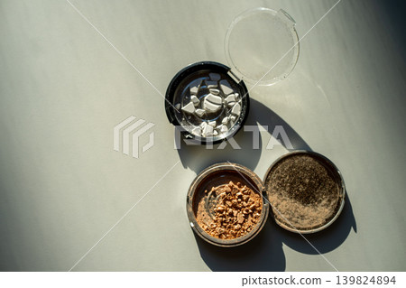Broken palettes with bronzer and powder on a white table. Decorative cosmetics Broken palettes with bronzer and powder on a white table. Decorative cosmetics 139824894