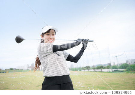 Image of a young, smiling woman swinging a driver at a golf driving range. Nice shot! Image of a young, smiling woman swinging a driver at a golf driving range. Nice shot! 139824995