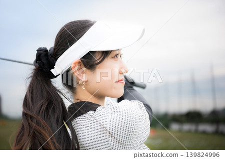 A sporty image of a young, smiling female golfer swinging a driver at a golf driving range, viewed from above. A sporty image of a young, smiling female golfer swinging a driver at a golf driving range, viewed from above. 139824996