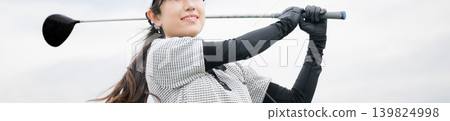 A young, smiling female golfer swings a driver at a driving range. (Banner with no face shown) 139824998