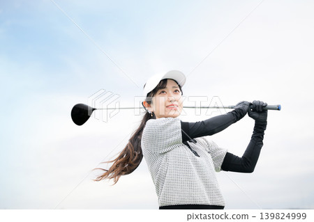 Image of a young, smiling woman swinging a driver at a golf driving range. Nice shot! Image of a young, smiling woman swinging a driver at a golf driving range. Nice shot! 139824999