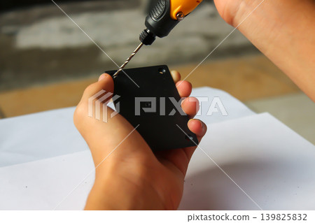 Close Up of Hands Using Electric Screwdriver to Assemble Black Plastic Device on White Background Close Up of Hands Using Electric Screwdriver to Assemble Black Plastic Device on White Background 139825832
