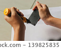 Close-up photo of a person using a small electric screwdriver to assemble or repair a black plastic electronic component on a clean white surface. Suitable for concepts related to DIY repair, 139825835