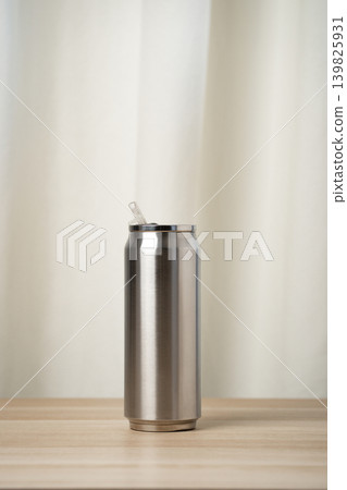 Stainless steel tumbler with a clear straw on a wooden table, minimalist and modern design. Portable insulated can for cold drinks, reusable and eco-friendly for everyday hydration and travel. 139825931