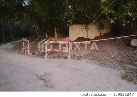 Construction has disturbed the ground near a wall, barriers and tape mark the area Construction has disturbed the ground near a wall, barriers and tape mark the area 139826247