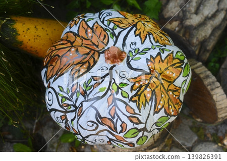 Painted pumpkin showing colorful autumn leaves and vine patterns lies in the garden Painted pumpkin showing colorful autumn leaves and vine patterns lies in the garden 139826391