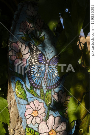 A colorful butterfly and flower design is painted on a tree trunk, outdoors A colorful butterfly and flower design is painted on a tree trunk, outdoors 139826392