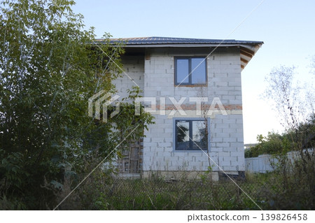 An unfinished two story house stands with windows and open doorway An unfinished two story house stands with windows and open doorway 139826458