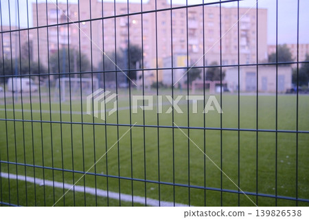 A fenced field has goalposts and white lines. Buildings are in the distance A fenced field has goalposts and white lines. Buildings are in the distance 139826538