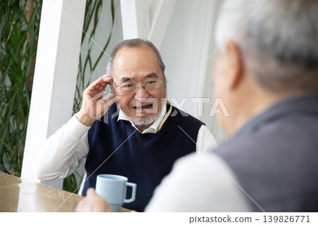 A senior Japanese man with hearing loss cannot hear his friends during conversations. A senior Japanese man with hearing loss cannot hear his friends during conversations. 139826771