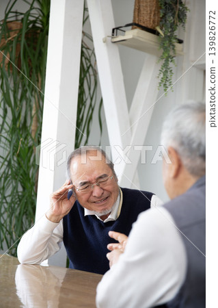 A senior Japanese man with hearing loss cannot hear his friends during conversations. A senior Japanese man with hearing loss cannot hear his friends during conversations. 139826772