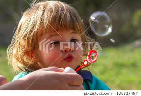 Happy Little Blonde Girl Playing with Floating Soap Bubbles Happy Little Blonde Girl Playing with Floating Soap Bubbles 139827467
