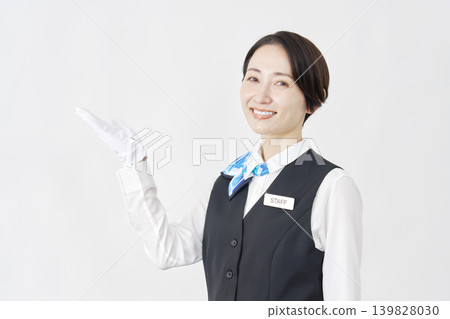 Female staff member pointing to the left with her palm; receptionist/bus guide; white background. Female staff member pointing to the left with her palm; receptionist/bus guide; white background. 139828030
