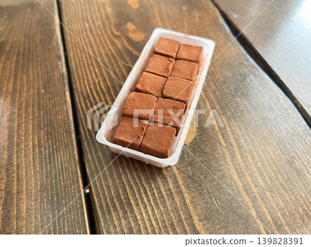 Square-shaped raw chocolate. Sweet chocolate mixed with fresh cream, packaged in a plastic container. Square-shaped raw chocolate. Sweet chocolate mixed with fresh cream, packaged in a plastic container. 139828391
