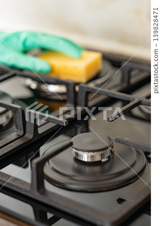 Cleaning a gas hob with a sponge and glove, removing grease in a modern kitchen. Cleaning a gas hob with a sponge and glove, removing grease in a modern kitchen. 139828471