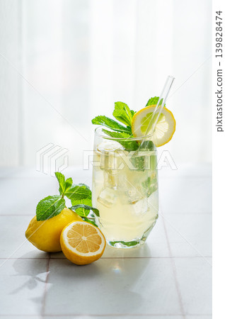 A summer drink with lemon, mint, and ice in a glass against a sunny window background. 139828474