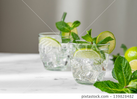 A fresh mojito with lime, mint and ice in glasses. Citrus lemonade or cocktail on a marble table A fresh mojito with lime, mint and ice in glasses. Citrus lemonade or cocktail on a marble table 139828482