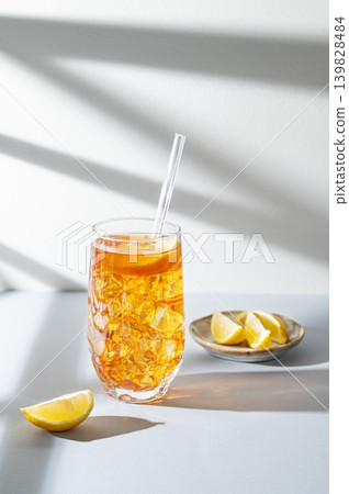 Iced tea with lemon in a glass on a light background with shadows and citrus fruits Iced tea with lemon in a glass on a light background with shadows and citrus fruits 139828484