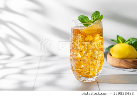 Iced tea with lemon and mint in a glass on a light tile background with shadows Iced tea with lemon and mint in a glass on a light tile background with shadows 139828488