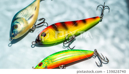 Colorful fishing lures and tackles on blue background with shadow from water, ready for fishing Colorful fishing lures and tackles on blue background with shadow from water, ready for fishing 139828740