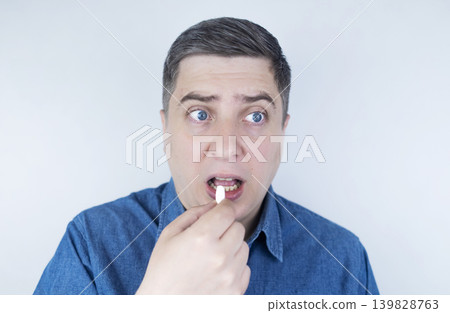 Man suffering from phagophobia struggling to swallow pill. Caucasian male looking anxious and scared before taking medication, experiencing fear of choking or swallowing difficulties. Man suffering from phagophobia struggling to swallow pill. Caucasian male looking anxious and scared before taking medication, experiencing fear of choking or swallowing difficulties. 139828763