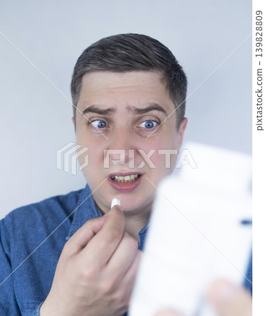 Man suffering from phagophobia struggling to swallow pill. Caucasian male looking anxious and scared before taking medication, experiencing fear of choking or swallowing difficulties. Man suffering from phagophobia struggling to swallow pill. Caucasian male looking anxious and scared before taking medication, experiencing fear of choking or swallowing difficulties. 139828809