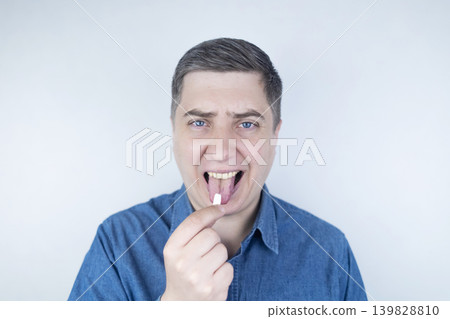 Man suffering from phagophobia struggling to swallow pill. Caucasian male looking anxious and scared before taking medication, experiencing fear of choking or swallowing difficulties.  139828810
