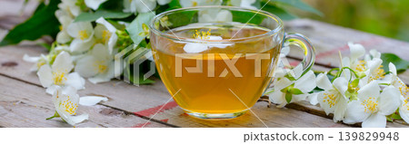 A cup of green tea with jasmine flowers on grunge wooden table outdoors 139829948