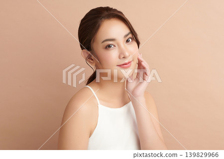 A beautiful young Asian woman with clean, fresh skin against a beige background. Skincare, facial treatment, cosmetology, beauty, and spa. An elegant portrait of an Asian woman. 139829966