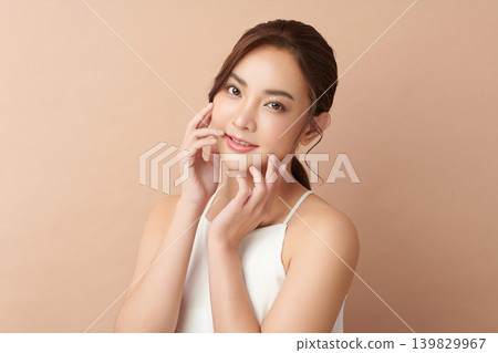 A beautiful young Asian woman with clean, fresh skin against a beige background. Skincare, facial treatment, cosmetology, beauty, and spa. An elegant portrait of an Asian woman. 139829967
