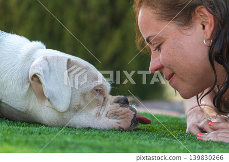 Young woman happily lying down with her boxer dog outdoors on grass Young woman happily lying down with her boxer dog outdoors on grass 139830266