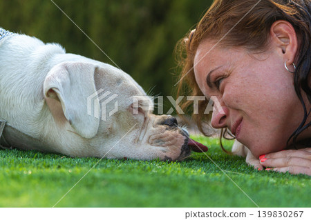 Smiling young woman relaxing on the grass with her boxer dog by her side Smiling young woman relaxing on the grass with her boxer dog by her side 139830267