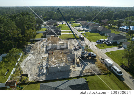 Lifting crane truck and builders working on roof construction of unfinished residential house with wooden frame structure in Florida suburban area. Housing development concept 139830634
