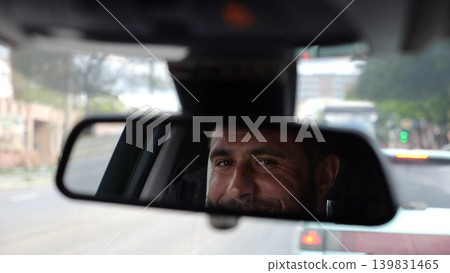 Eyes of male smiling driver reflecting in rearview mirror while riding motor auto. Young man looking concentrated to urban road during operating vehicle. Confident guy driving modern car at city Eyes of male smiling driver reflecting in rearview mirror while riding motor auto. Young man looking concentrated to urban road during operating vehicle. Confident guy driving modern car at city 139831465