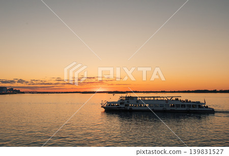 People enjoy an evening cruise aboard a passenger boat on the wide Volga River. Sunset illuminate the sky and reflect beautifully on the water 139831527