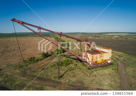 Aerial view of giant dragline excavator stands abandoned in a wide open area surrounded by fields with sparse vegetation and dirt roads Aerial view of giant dragline excavator stands abandoned in a wide open area surrounded by fields with sparse vegetation and dirt roads 139831569